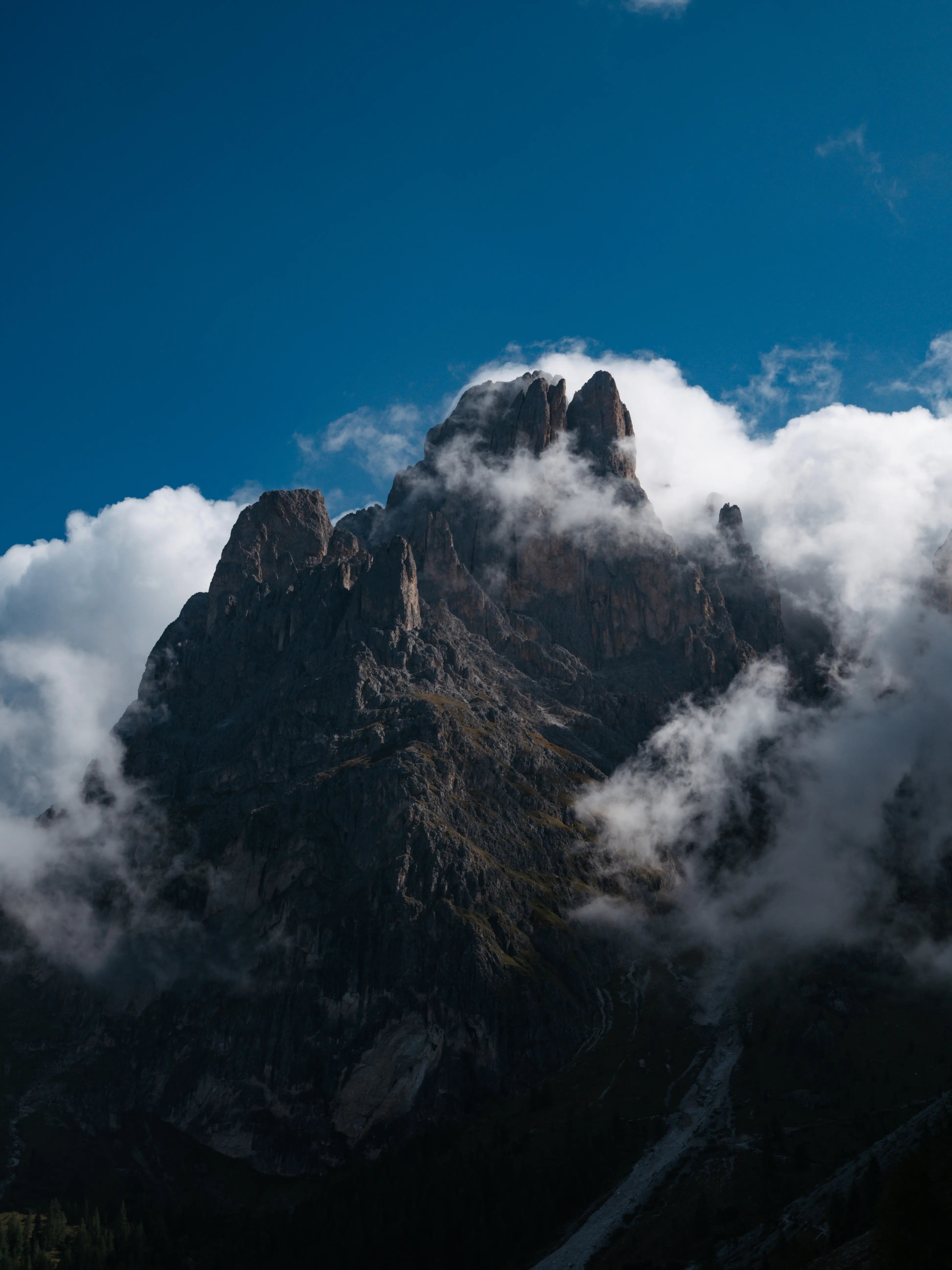 Mountain peak partially obscured by clouds under a clear blue sky
